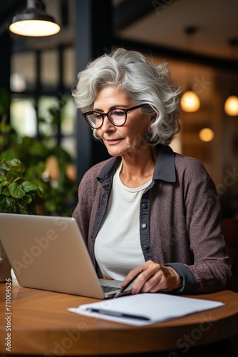 A thoughtful senior woman works on her laptop in a cafe