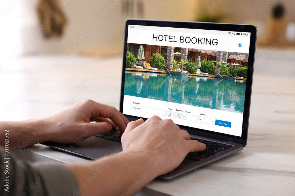 Man using laptop to book hotel at white table, closeup Man using laptop to book hotel at white table, closeup