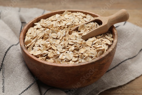 Bowl and scoop with oatmeal on wooden table, closeup