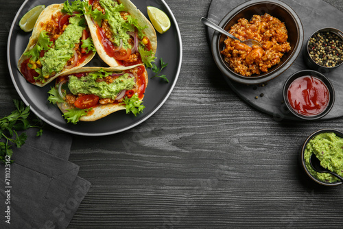 Delicious tacos with guacamole, meat and vegetables on wooden table, flat lay. Space for text