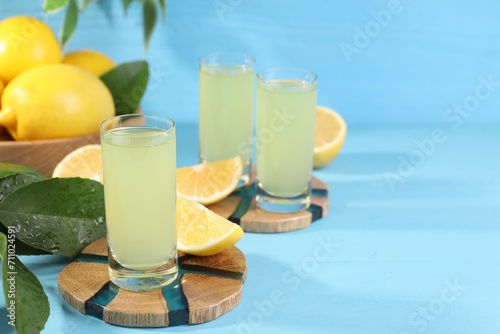 Tasty limoncello liqueur, lemons and green leaves on light blue table, space for text