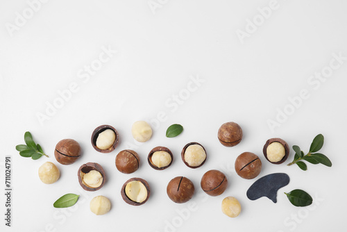 Tasty Macadamia nuts and green leaves on white background, flat lay. Space for text