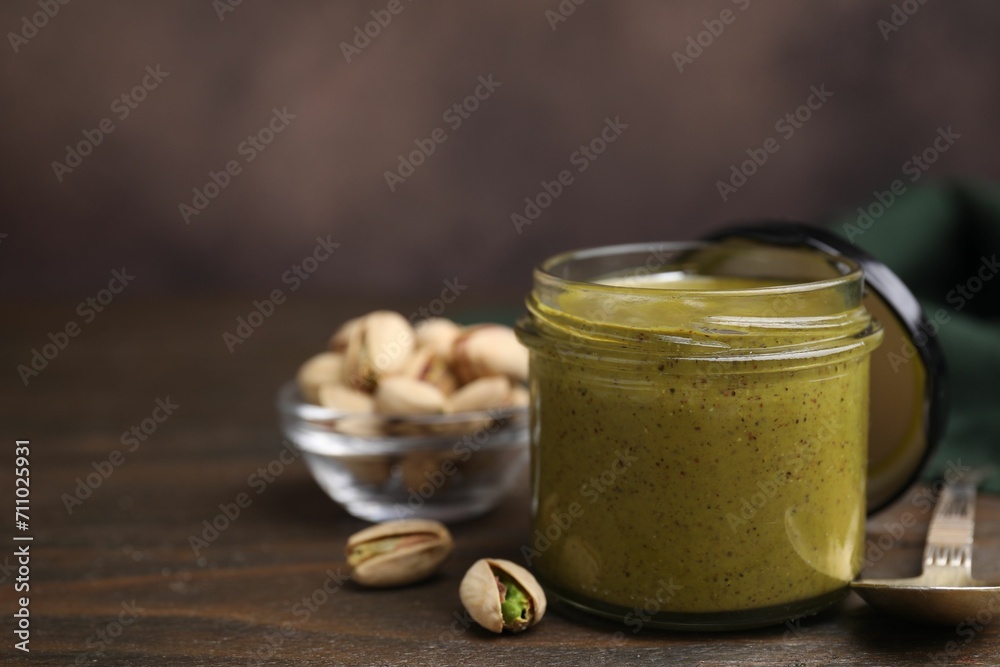 Tasty pistachio cream in jar, spoon and nuts on wooden table, closeup. Space for text Tasty pistachio cream in jar, spoon and nuts on wooden table, closeup. Space for text