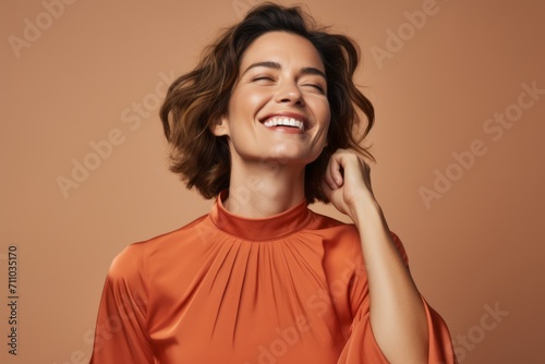Cheerful young woman with closed eyes in orange dress on brown background