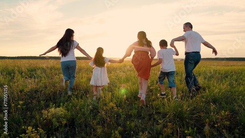 Parents, children run hand in hand across field at sunset. Family, children play, run together, travel in nature. Mom, dad, children run through meadow, family dream of fly. Father mother son daughter