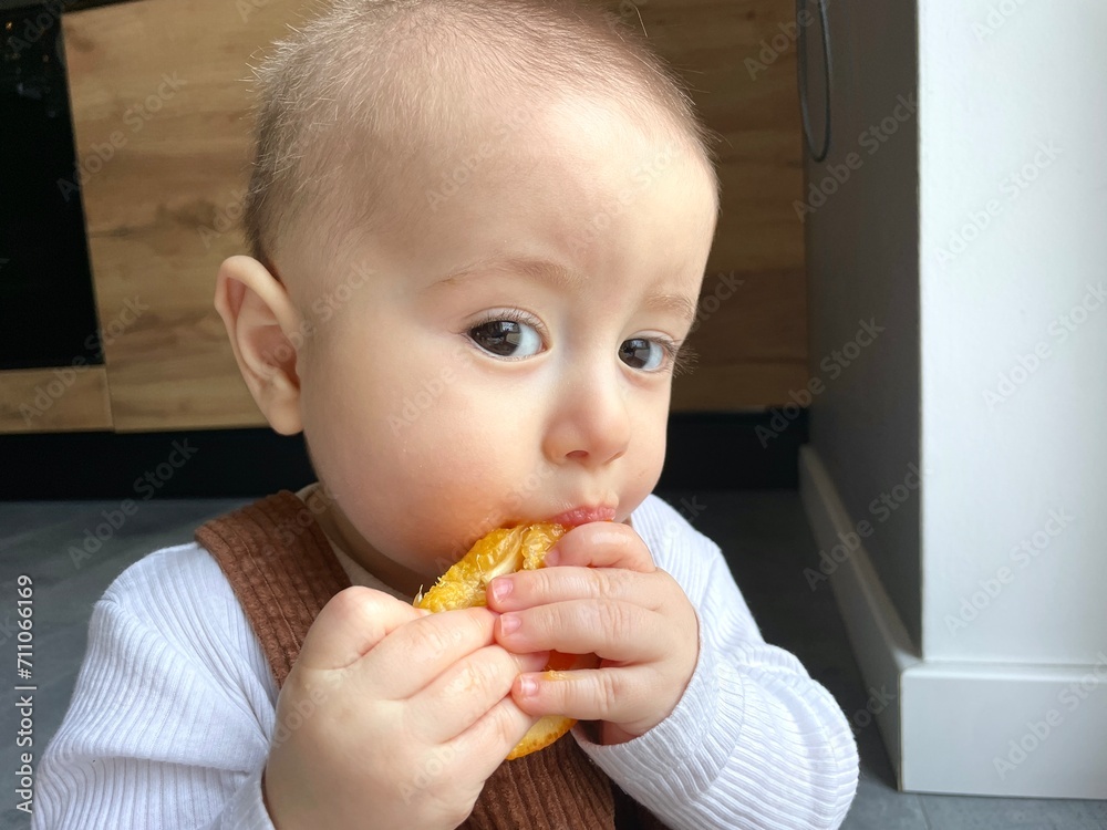 A little boy eats a piece of orange by himself A little boy eats a piece of orange by himself