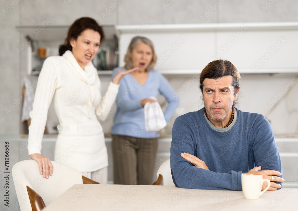 Fototapeta premium Wife and elderly mother actively prove something to man in kitchen