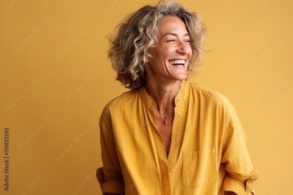 Portrait of a happy mature woman laughing and looking up over yellow background Portrait of a happy mature woman laughing and looking up over yellow background