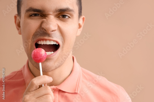 Handsome young man with lollipop on brown background. Dental care concept
