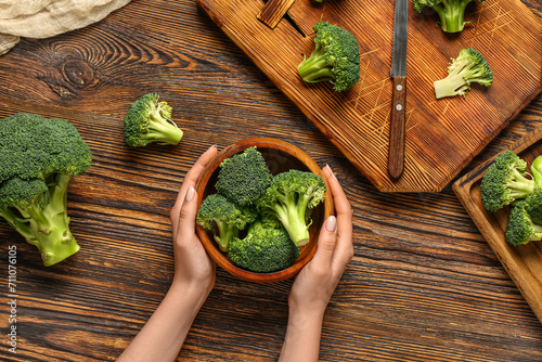 Female hands with bowl of fresh broccoli cabbages on wooden background