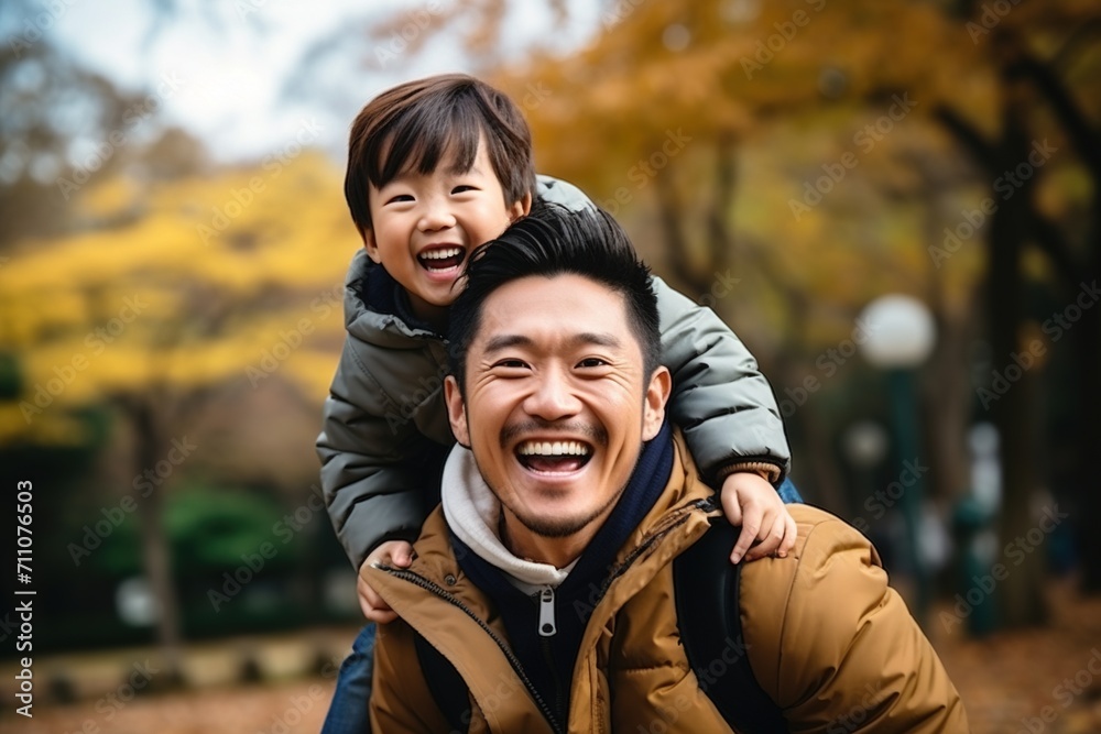 Happy Asian Father Carrying His Son on His Back in the Park Happy Asian Father Carrying His Son on His Back in the Park