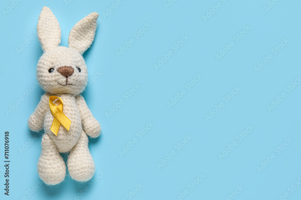 Obraz premium Toy bunny with golden ribbon on blue background. Childhood cancer awareness concept