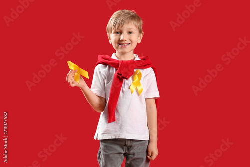 Cute little boy with yellow ribbons on red background. Childhood cancer awareness concept