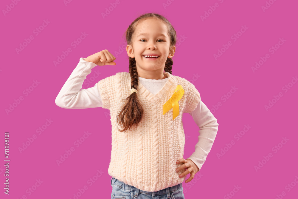 Cute little girl with yellow ribbon showing muscles on purple background. Childhood cancer awareness concept Cute little girl with yellow ribbon showing muscles on purple background. Childhood cancer awareness concept