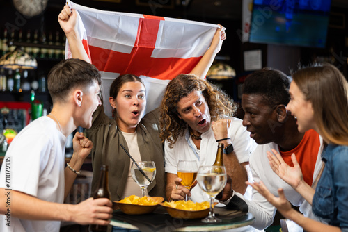 Billede på lærred Group of cheerful football fans rooting for England team together in sports bar,