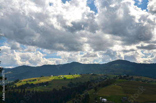 Green fields and hills with houses, high mountain ridge in a distance. Carpathian Mountains, Ukraine