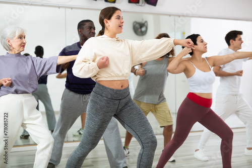Smiling young woman rehearsing modern dance with group in dance school