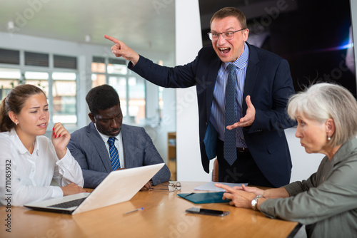 Moody middle-aged man boss complaining team about mistake. Businessman managers pointing out mistakes to team. Toxic work environment concept photo