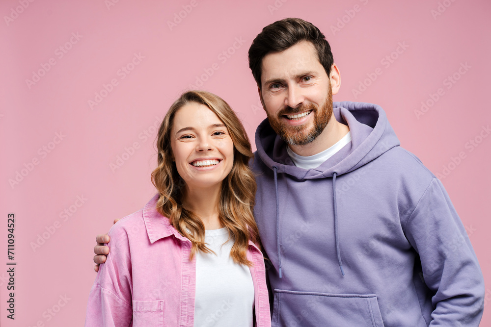 Portrait of attractive smiling couple hugging isolated on pink background. Happy bearded man and beautiful woman wearing stylish casual clothing looking at camera in studio Portrait of attractive smiling couple hugging isolated on pink background. Happy bearded man and beautiful woman wearing stylish casual clothing looking at camera in studio