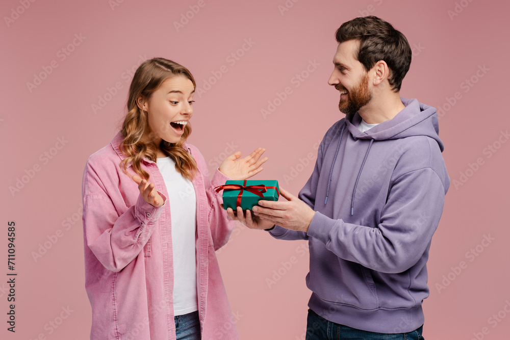 Smiling man giving gift box to overjoyed beautiful woman. Portrait of happy romantic couple celebration birthday isolated on pink background. Dating, love, Valentines day Smiling man giving gift box to overjoyed beautiful woman. Portrait of happy romantic couple celebration birthday isolated on pink background. Dating, love, Valentines day