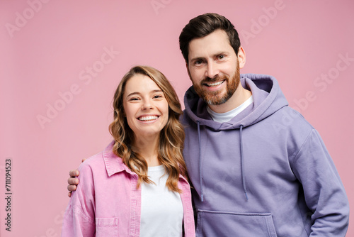 Portrait of attractive smiling couple hugging isolated on pink background. Happy bearded man and beautiful woman wearing stylish casual clothing looking at camera in studio 