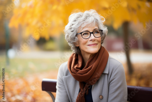 A Senior Woman with a Curly Gray Bob, Wearing a Glasses Chain, Sits on a Park Bench, Reflecting on Life as Autumn Leaves Fall Around Her