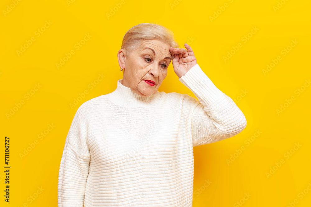 old tired grandmother in a white sweater is sad and suffers from pressure and headache on a yellow isolated background, elderly woman holds her head with her hand in depression old tired grandmother in a white sweater is sad and suffers from pressure and headache on a yellow isolated background, elderly woman holds her head with her hand in depression