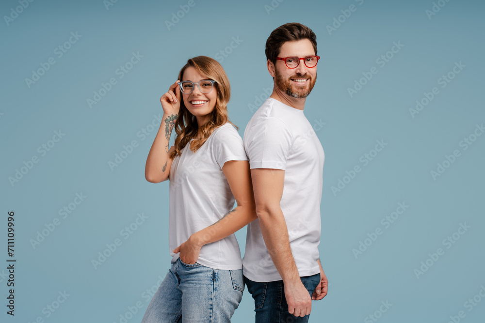 Naklejka premium Portrait of attractive smiling man and woman wearing white t shirt and stylish eyeglasses isolated on blue background. Happy confident fashion models posing for pictures in studio