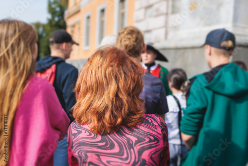 Group of students and school pupils on outdoor excursion tour in the city streets with guide, a docent with a tourist adult visitors, school field trip, urban tour in the summer sunny day