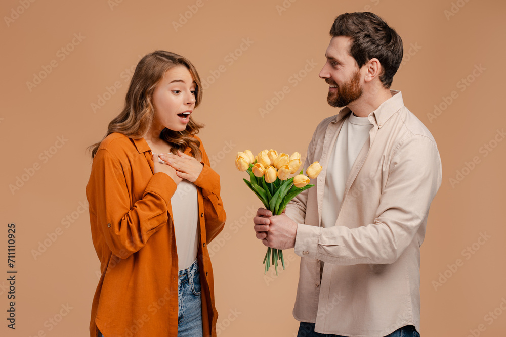 Smiling latin man giving bouquet of beautiful tulips flowers for young surprised woman. Happy romantic couple celebration birthday isolated on background. Dating, love, woman's day Smiling latin man giving bouquet of beautiful tulips flowers for young surprised woman. Happy romantic couple celebration birthday isolated on background. Dating, love, woman's day