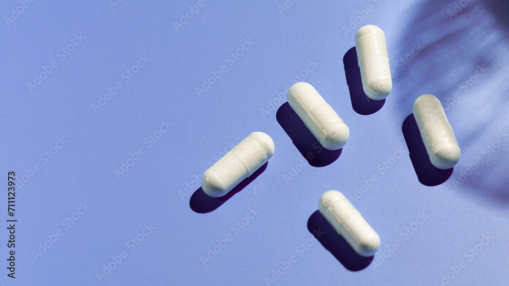 White capsules with vitamins or a dietary supplement on a purple background. Medicine, medicines White capsules with vitamins or a dietary supplement on a purple background. Medicine, medicines