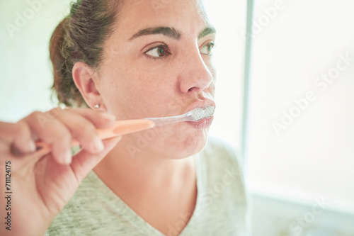 Young woman brushing teeth looking at mirror at home bathroom.  Dental care and hygiene