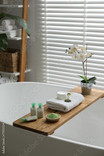 Wooden tray with spa products and orchid flowers on bath tub in bathroom