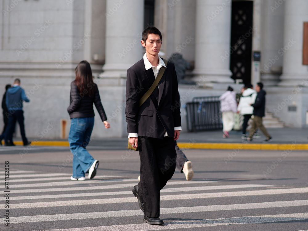 Portrait of handsome Chinese young man with black short hair wearing black blazer walking on street with modern city building background in sunny winter day, male fashion, cool Asian young man. Portrait of handsome Chinese young man with black short hair wearing black blazer walking on street with modern city building background in sunny winter day, male fashion, cool Asian young man.