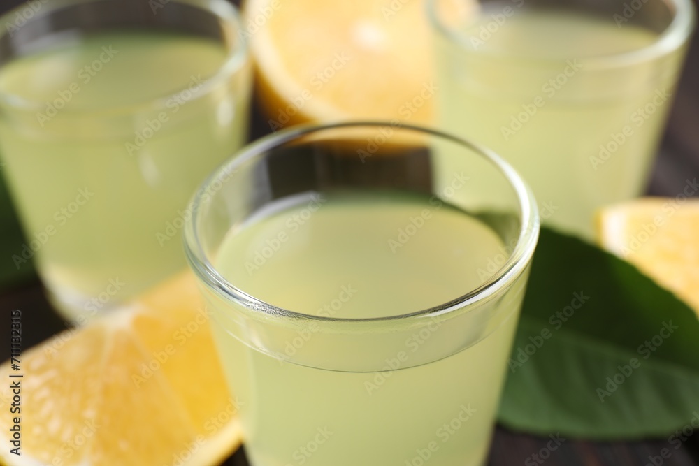 Tasty limoncello liqueur, lemon and green leaf on table, closeup