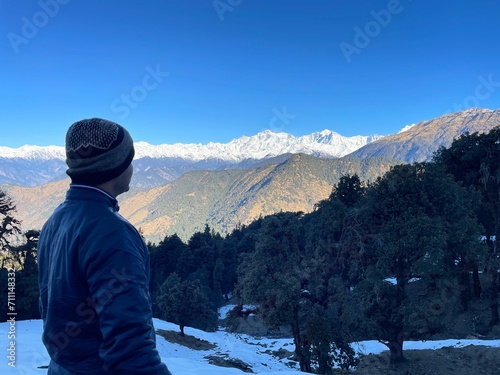 man looking into the distance at snowy mountains in nepal, surrounded by green trees