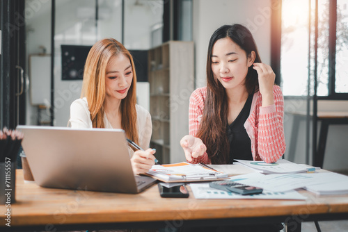 Happy multiethnic smiling business women working together in office, using calculator and laptop computer to calculate financial report.