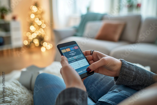 Close-up of hands holding a smartphone with a shopping app open, cozy home interior with Christmas tree in background. 