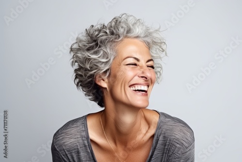 Portrait of a happy senior woman laughing against a grey background.