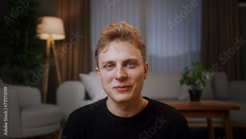 Close up portrait young blonde man sit on floor at home looking at camera wave hand greeting, talking to friend, chatting by webcam. Virtual meeting remotely, video call event concept 