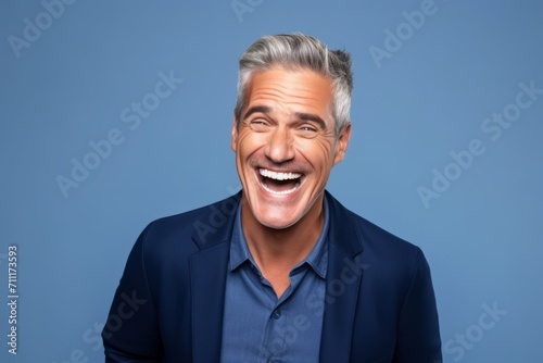 Handsome mature man laughing and looking at camera on blue background