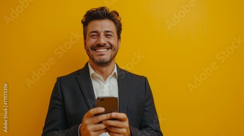 Businessman smiles happily while looking at mobile phone with a bright yellow background photo