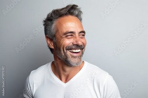 Portrait of a happy mature man laughing and looking at camera against grey background