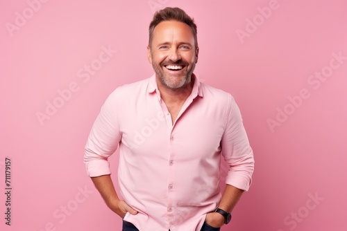 Portrait of a happy mature man standing with hands in pockets against pink background © Inigo