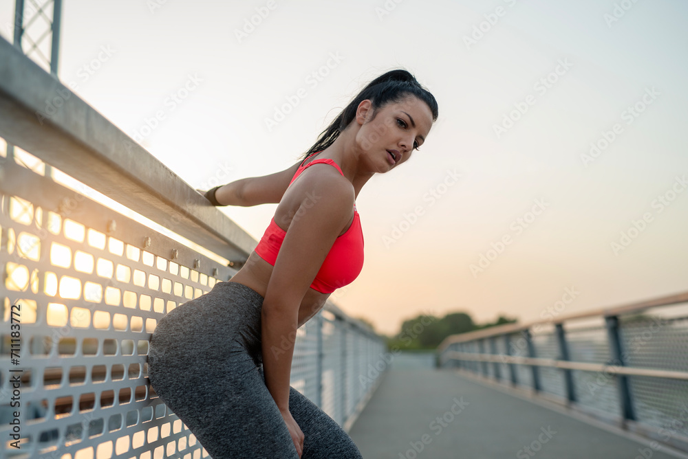 Attractive confident fitness girl posing on the bridge at sunset  