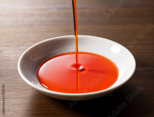 Pour chili oil sauce into a ceramic dish. Wooden background. Table.
