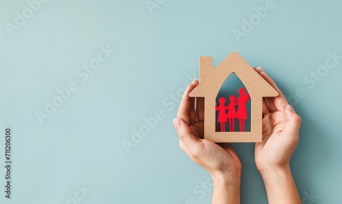 Nurturing Dreams: Woman's Hand Holding Wooden House with Red Paper Family, Top View on Light Blue Background, feelings of warmth, safety, and love