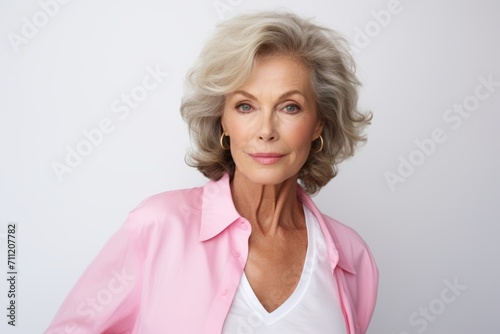Portrait of beautiful senior woman in pink jacket against grey background.