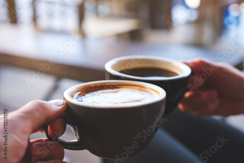 Closeup image of a couple people clinking coffee mugs in cafe