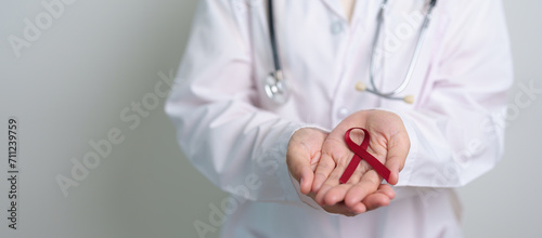 Doctor with Burgundy Red Ribbon for March multiple myeloma Cancer and December World Aids Day Awareness month. Healthcare and world cancer day concept